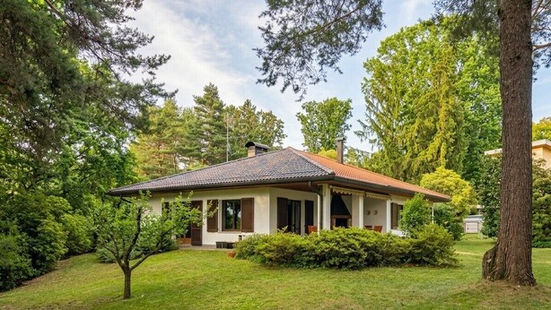 A single-story house with a tiled roof, surrounded by a well-maintained lawn and trees.