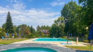 A swimming pool area with stone flooring, lounge chairs, and umbrellas.