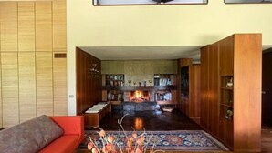 Een moderne woonkamer met een open haard, boekenkasten en een rode bank.