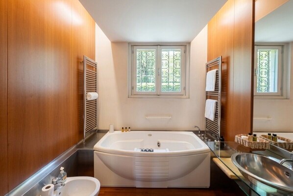 A modern bathroom with a large bathtub, a separate sink, and a window with decorative glass panes.