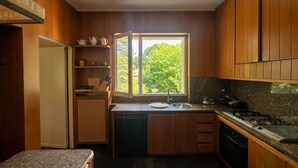 A compact kitchen with wooden cabinets, a built-in dishwasher, a window with a view of greenery, and a countertop with a sink and stove.