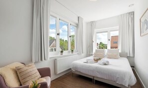 Ein Schlafzimmer mit Bett, Fenster, Heizkörper, Stuhl und Pflanze.