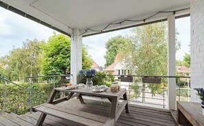Ein überdachter Außenbereich mit einem Holztisch, gedeckt für ein Essen, umgeben von Grünpflanzen und einer weißen Backsteinmauer.