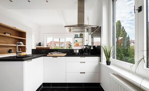 Eine moderne Küche mit weißen Schränken, einer schwarzen Arbeitsplatte und einem großen Fenster mit Blick auf Häuser.