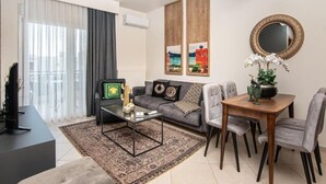 A modern living room with a sofa, coffee table, and dining table. - Alexandra Residence Seaside (ALEXANDROUPOLIS)