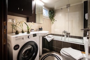 A compact bathroom with a washing machine, a sink, a bathtub, and a mirror.