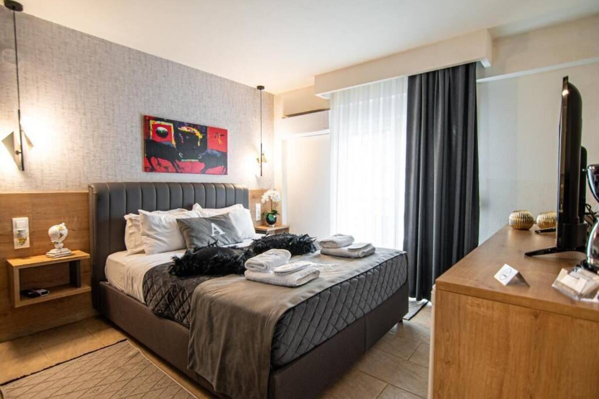 Une chambre d’hôtel moderne avec un grand lit, un bureau, une table de chevet, un tableau au mur et une fenêtre avec des rideaux.