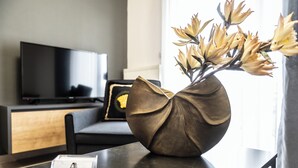 A modern room with a dark wooden table, a vase with flowers, a television, and a sofa. - Alexandra Residence Seaside (ALEXANDROUPOLIS)