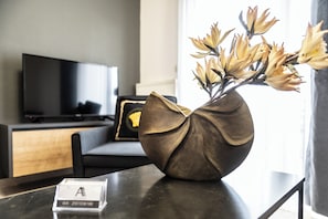 A modern room with a dark wooden table, a vase with flowers, a television, and a sofa.