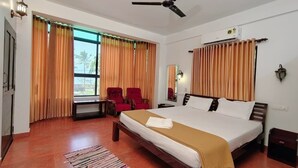 A bedroom with a bed, a ceiling fan, a window with curtains, a red chair, and a bedside table. - Samudra Heritage (Kochi)