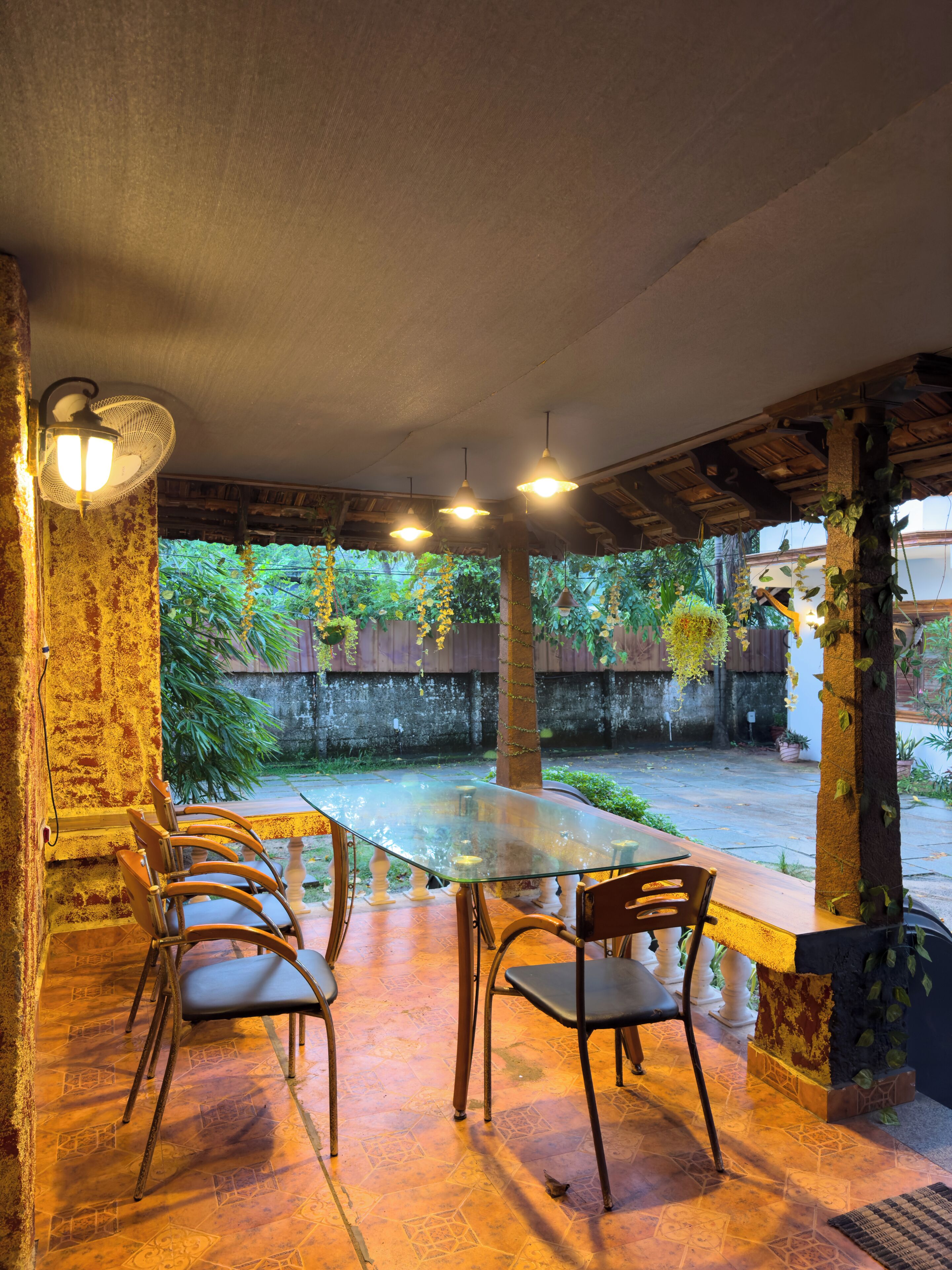 Un espacio de comedor al aire libre con una mesa y sillas de vidrio, rodeado de plantas y vistas a un jardín.