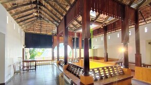 A spacious room with a wooden ceiling, a central table, and chairs. - Samudra Heritage (Kochi)