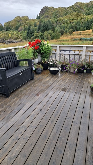 A wooden deck with a black bench, potted plants, and a view of a mountainous landscape. - Cosy cottage by the sea, Ballstad (Vestvågøy)