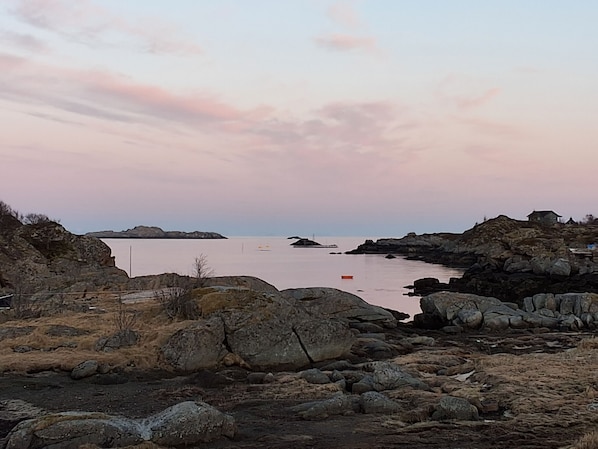 A rocky shoreline with a calm body of water, a small boat, and a distant island.