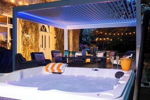 Ein Whirlpool unter einer überdachten Terrasse mit Stühlen und einem Tisch, umgeben von Lichterketten.