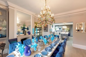 A dining room with a long table, blue upholstered chairs, a chandelier, and a fireplace.