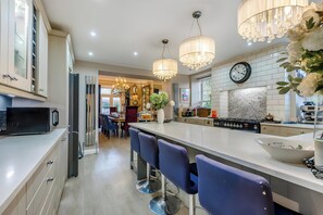 A modern kitchen with a central island, bar stools, a refrigerator, and a dining area in the background.
