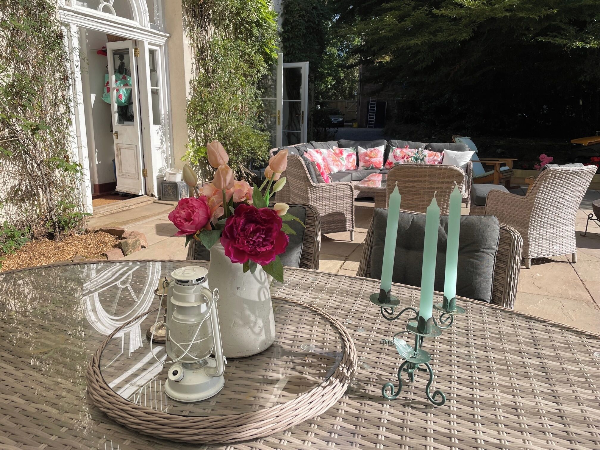 A wicker table with a glass top, a white vase with flowers, and a candle holder.