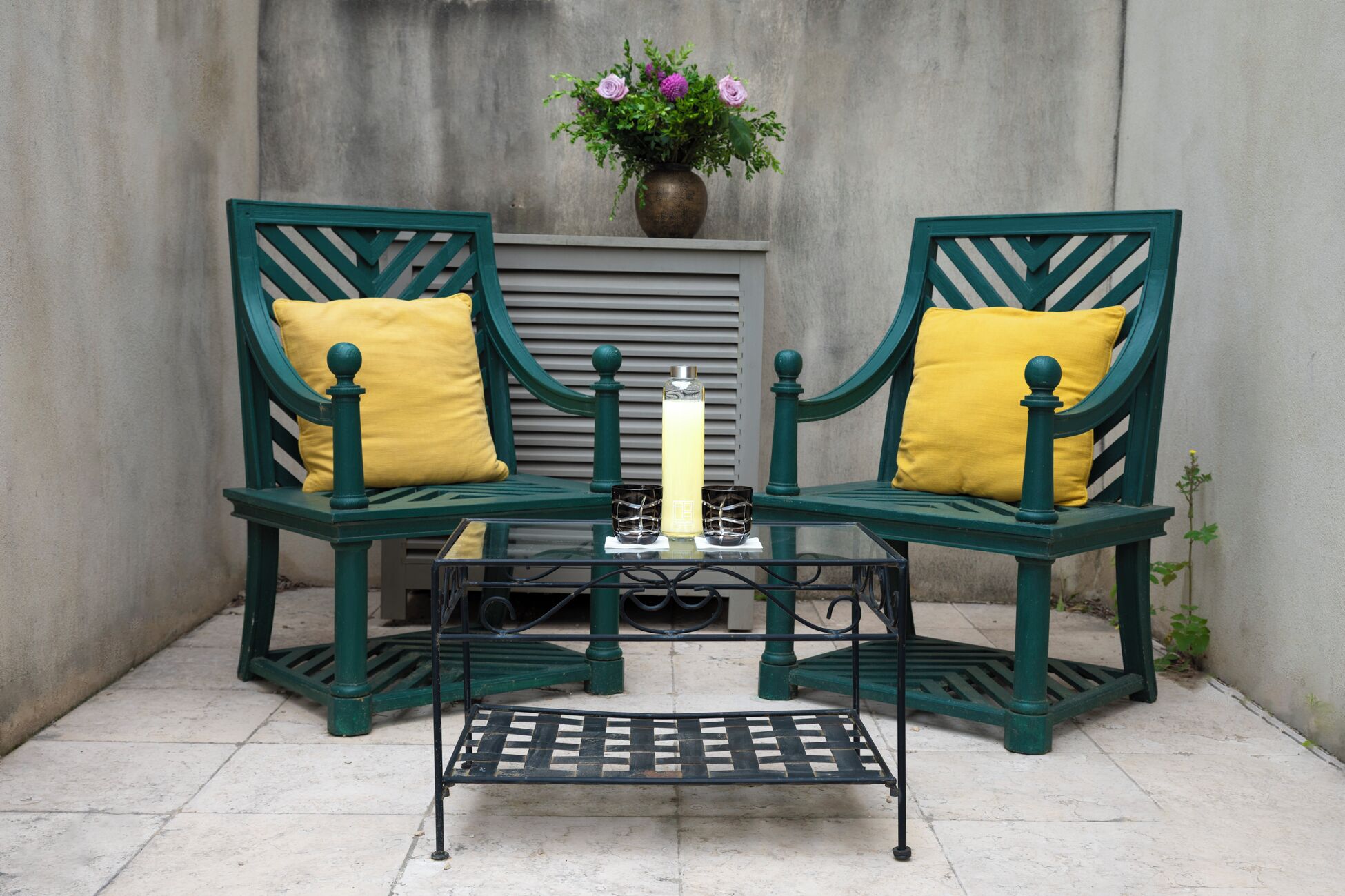 Two green chairs with yellow cushions, a table with a candle, and a vase with flowers.