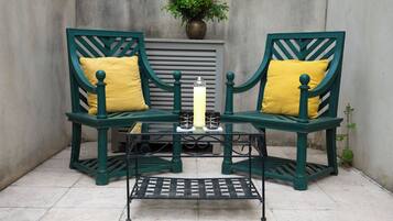 Two green chairs with yellow cushions, a table with a candle, and a vase with flowers.