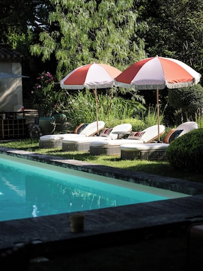 Un espace aménagé au bord de la piscine, avec des chaises longues et des parasols, le tout entouré de verdure.
