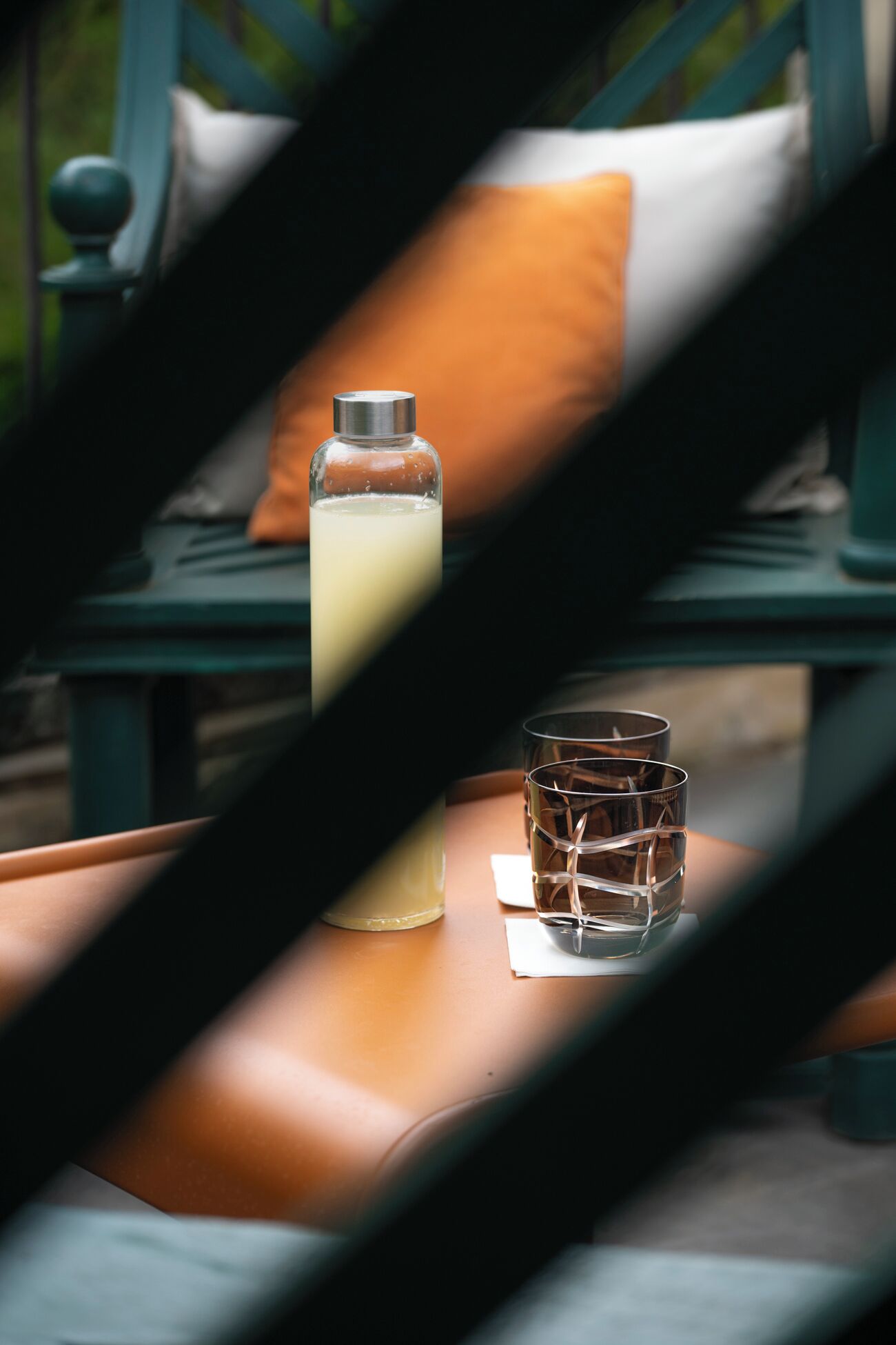 A bottle and a glass on a chair with a cushion.