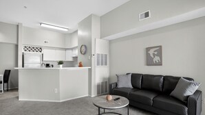 Un espacio habitable moderno con cocina, un sofá de cuero negro y una mesa de centro redonda.