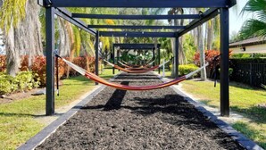 Una hamaca bajo una pérgola en un jardín con palmeras y acolchado.