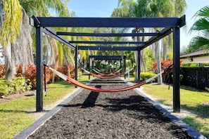 Eine Hängematte unter einer Pergola in einem Garten mit Palmen und Mulch.