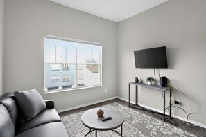 Ein modernes Wohnzimmer mit einer Couch, einem Couchtisch, einem an der Wand montierten Fernseher und einem großen Fenster.