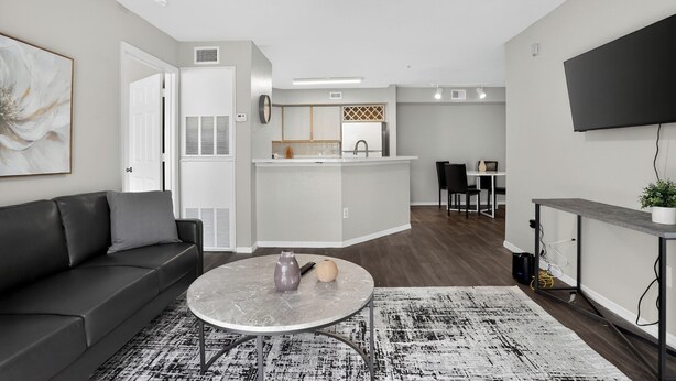Een moderne woonkamer met een bank, salontafel en kunstwerk. Achtergrond toont een keuken en eetgedeelte.