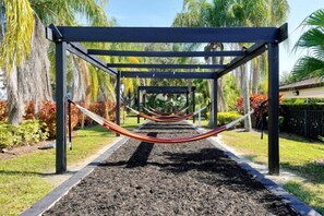 Una hamaca bajo una pérgola en un jardín con palmeras y acolchado.