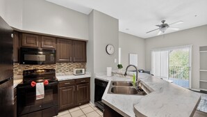 A modern kitchen with dark wood cabinets, a black stove, a microwave, and a large island with a sink. - Chic 2BR Retreat Near Attractions (Orlando)