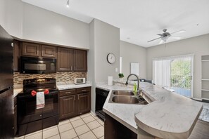 Une cuisine moderne avec des meubles de couleur bois foncé, une cuisinière noire, un four à micro-ondes et un grand îlot central doté d’un évier.