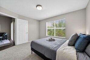 Ein Schlafzimmer mit einem Bett, einem Fenster mit Jalousien, einer Tür und einer kleinen Sitzecke mit Tisch und Stuhl.