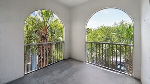 A balcony with two arched windows, a metal railing, and a view of palm trees and greenery. - Chic 2BR Retreat Near Attractions (Orlando)
