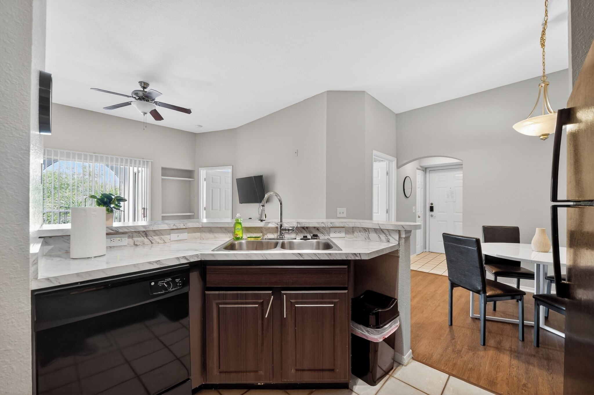 A modern kitchen with a built-in dishwasher, a sink, and a ceiling fan.