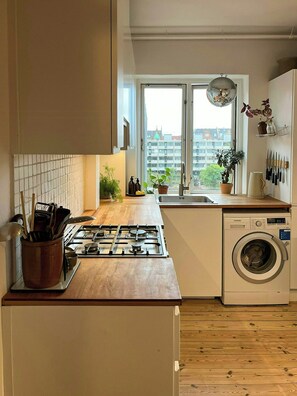 Una cocina con estufa a gas, lavadora y ventana con vista a edificios.