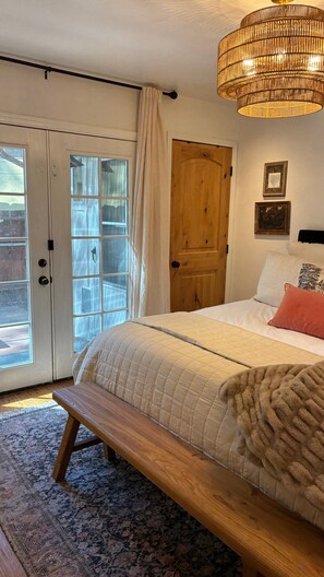 Ein Schlafzimmer mit Bett, Sitzbank, Holztür und einem großen Fenster.