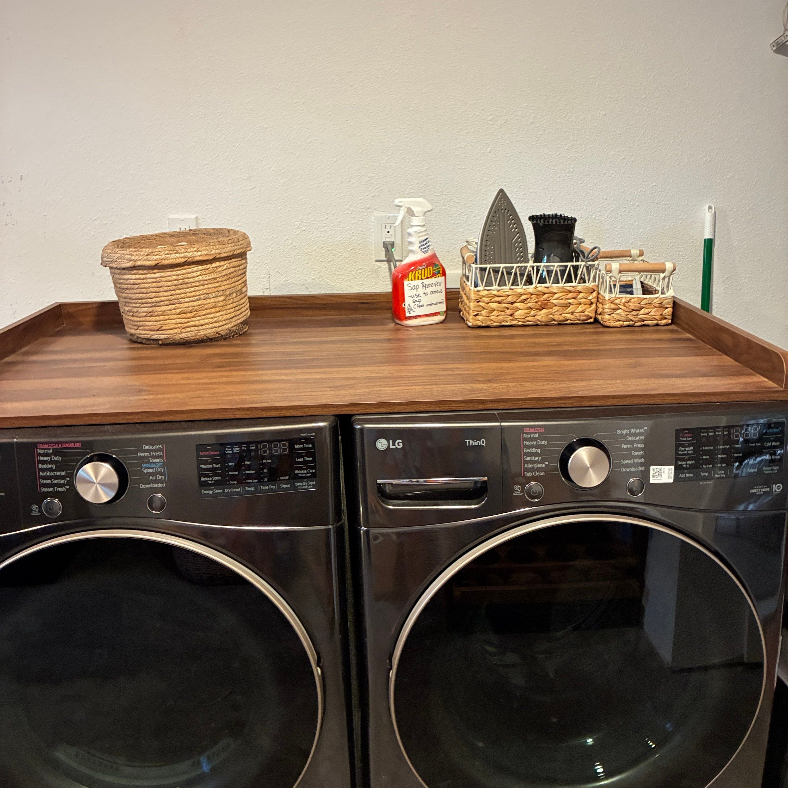 Deux lave-linge à chargement frontal LG ThinQ, avec un plan de travail en bois placé au-dessus.