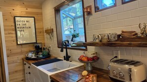 Eine kleine Küche mit Spüle, Toaster, Obstschale und einem Fenster mit Blick auf Bäume.