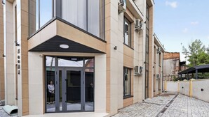 Un edificio moderno con entrada de vidrio, fachada beige y gris, y unidades de aire acondicionado.