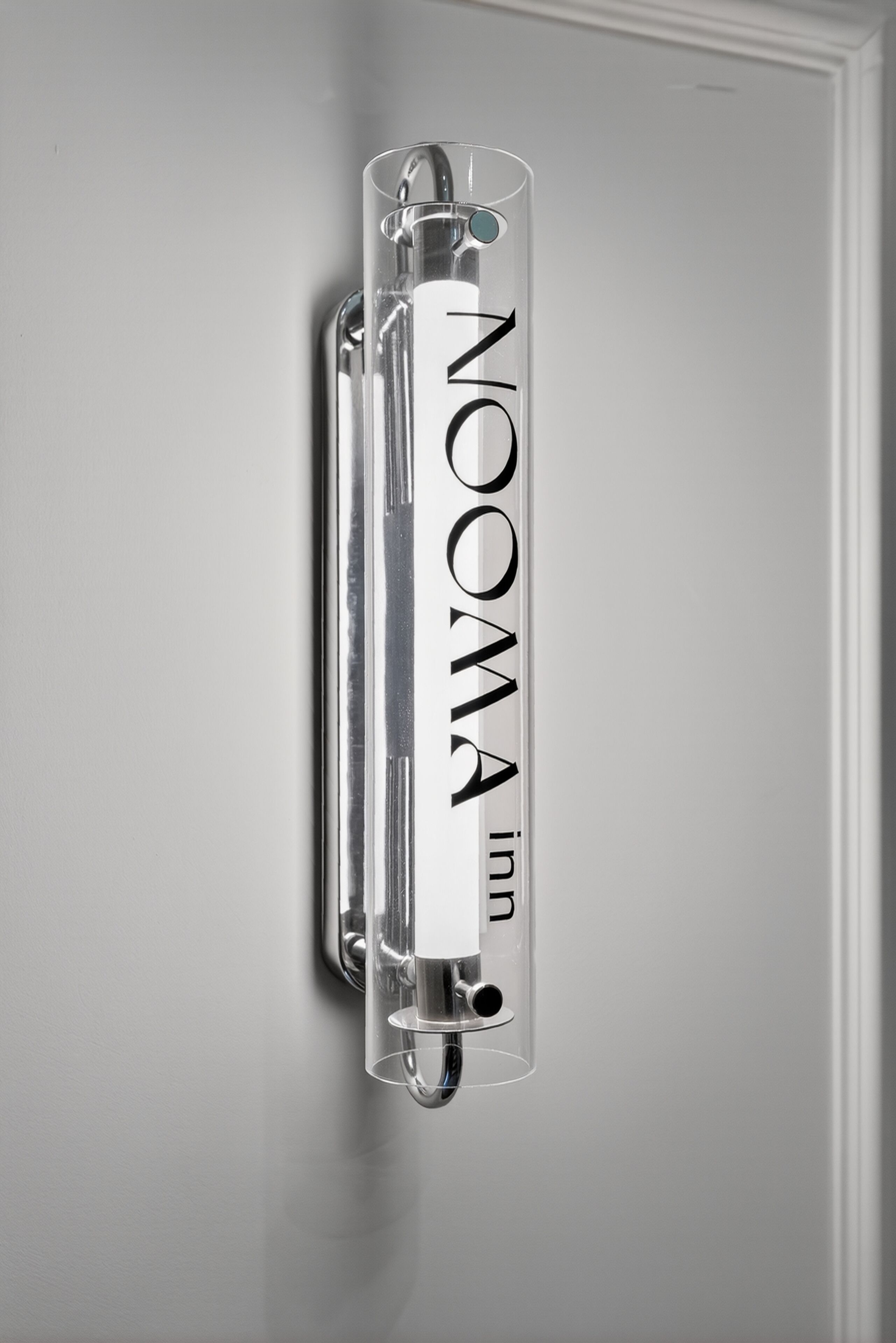 A clear, cylindrical object with the text 'NOOMA inn' on it, mounted on a wall.