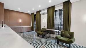 Una habitación de hotel moderna con espacio para la cocina, una mesa de comedor, dos sillones verdes y suelo con estampado.
