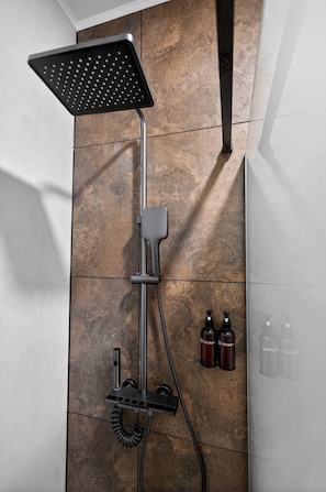 Ducha con cabezal de mano, panel de control en la pared y dos botellas de champú y acondicionador.