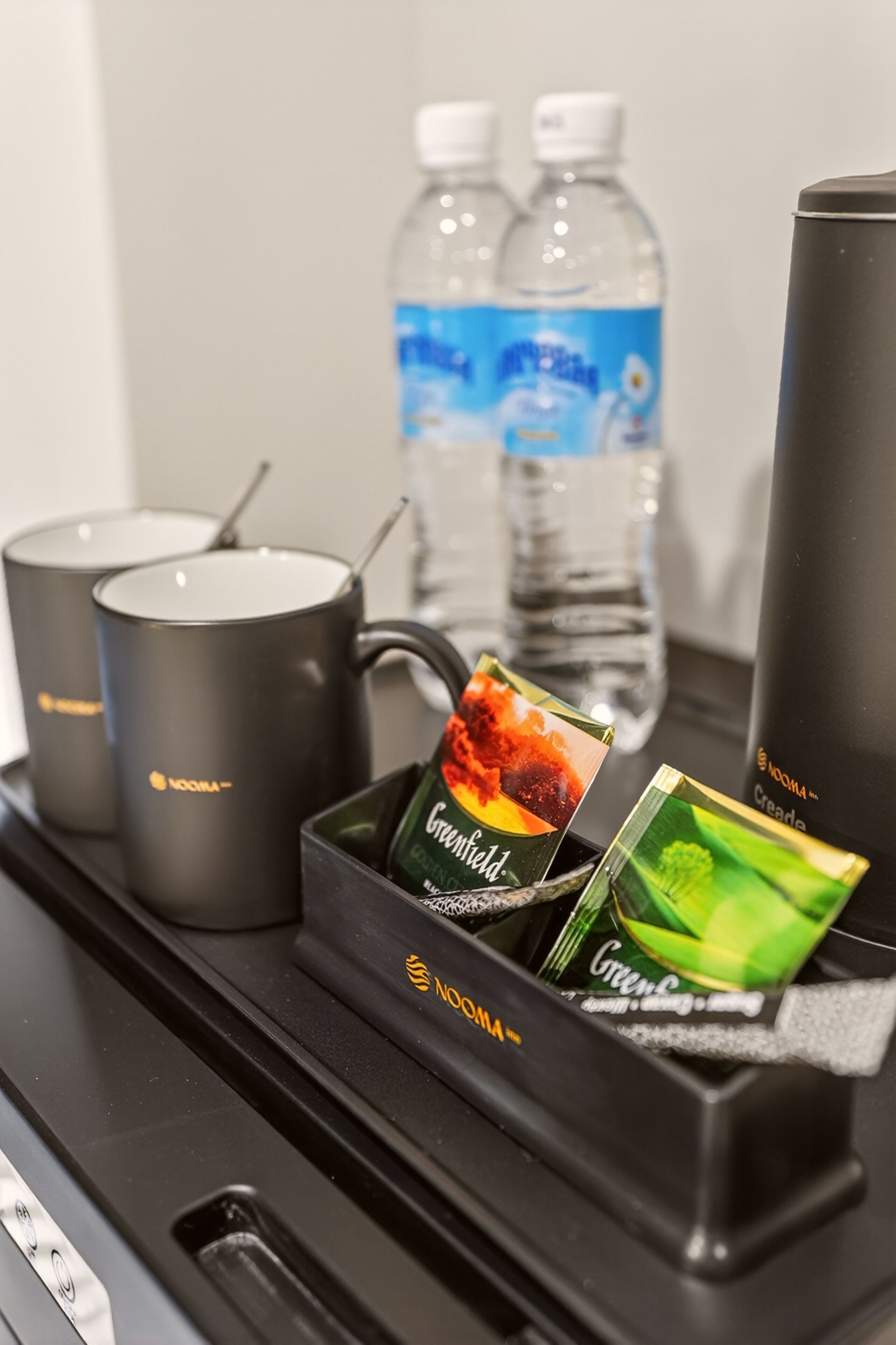 A tray with a coffee maker, two water bottles, a thermos, and two packets of instant coffee.