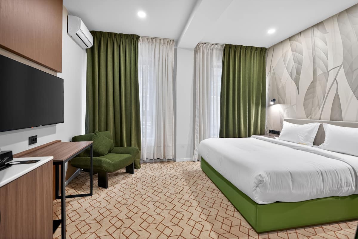 Habitació d'hotel amb llit, escriptori, cadira, televisió i cortines.