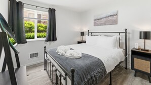 Een slaapkamer met een bed, een raam met gordijnen, een nachtkastje met een lamp en een schilderij aan de muur.