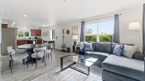 Een moderne woonkamer met een glazen salontafel, een grijze bank en een eethoek met stoelen.