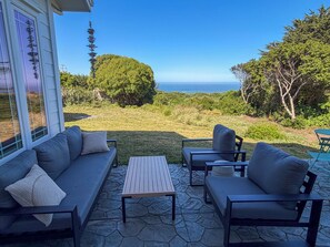 Eine Terrasse mit einer Couch, Stühlen und einem Tisch, mit Blick auf eine Rasenfläche und den Ozean.